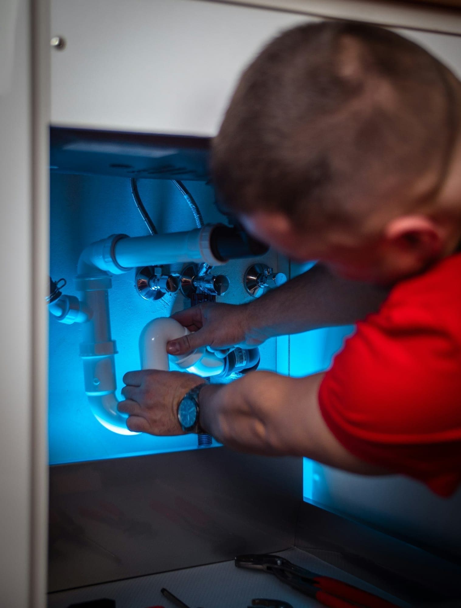 Plumber fixing pipework in a cabinet under a sink