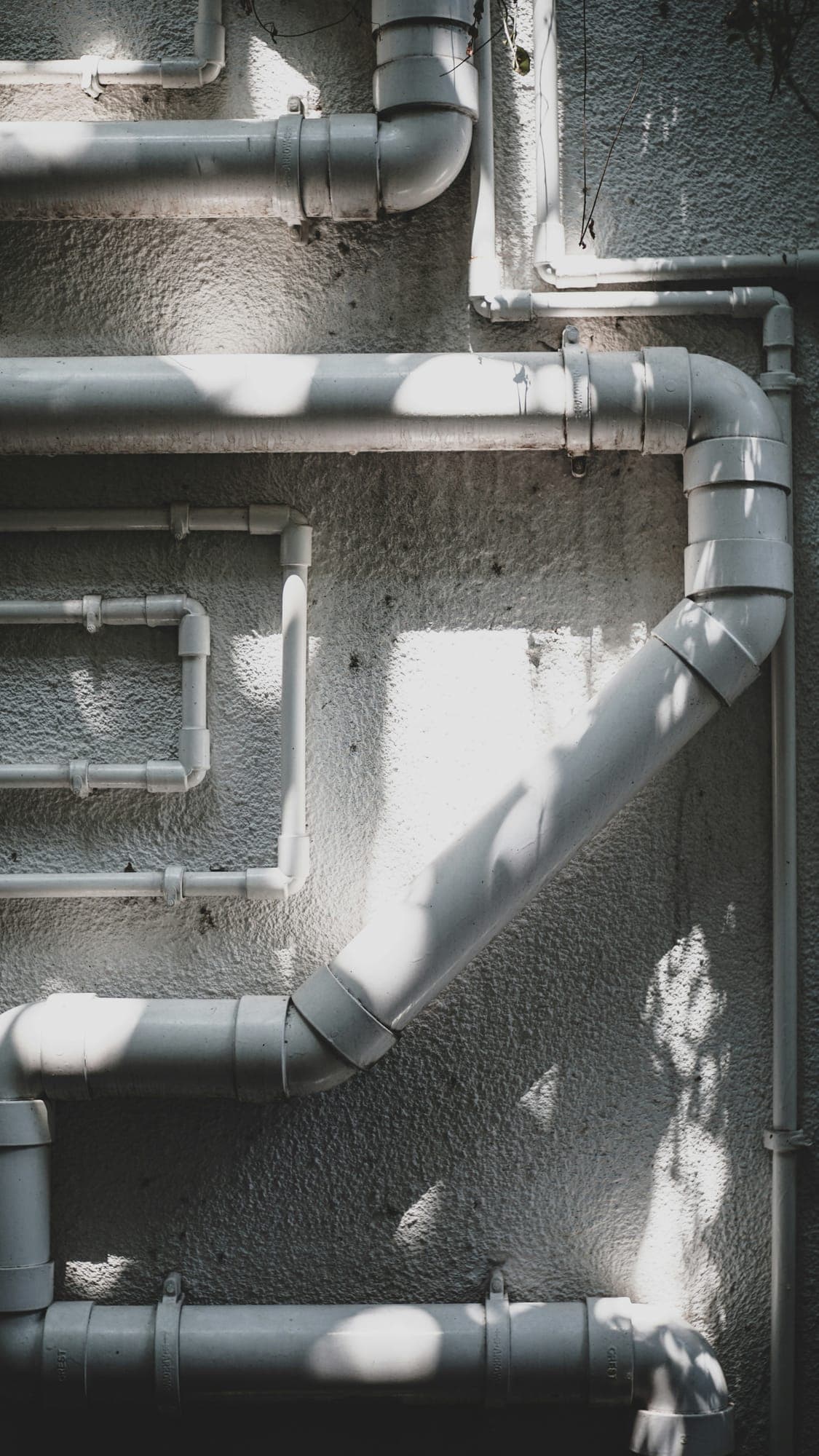 White uPVC pipes and bends running across a textured wall